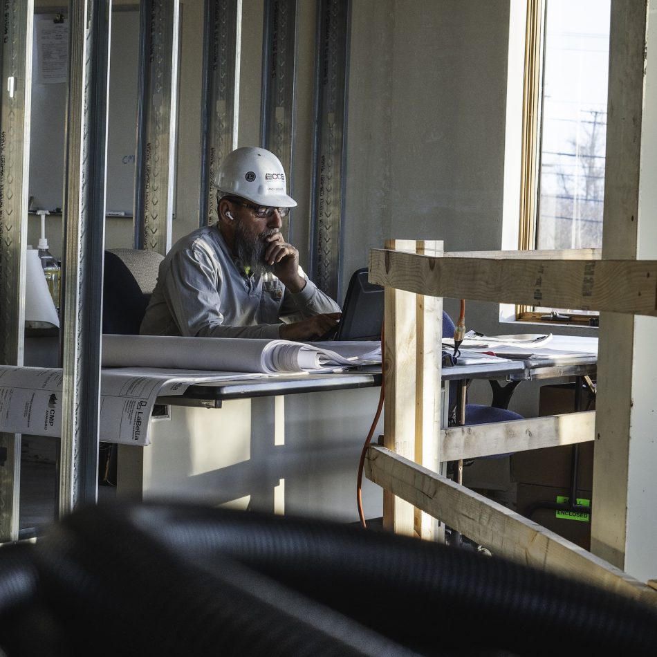 A worker in a hard hat at a desk looking at a computer