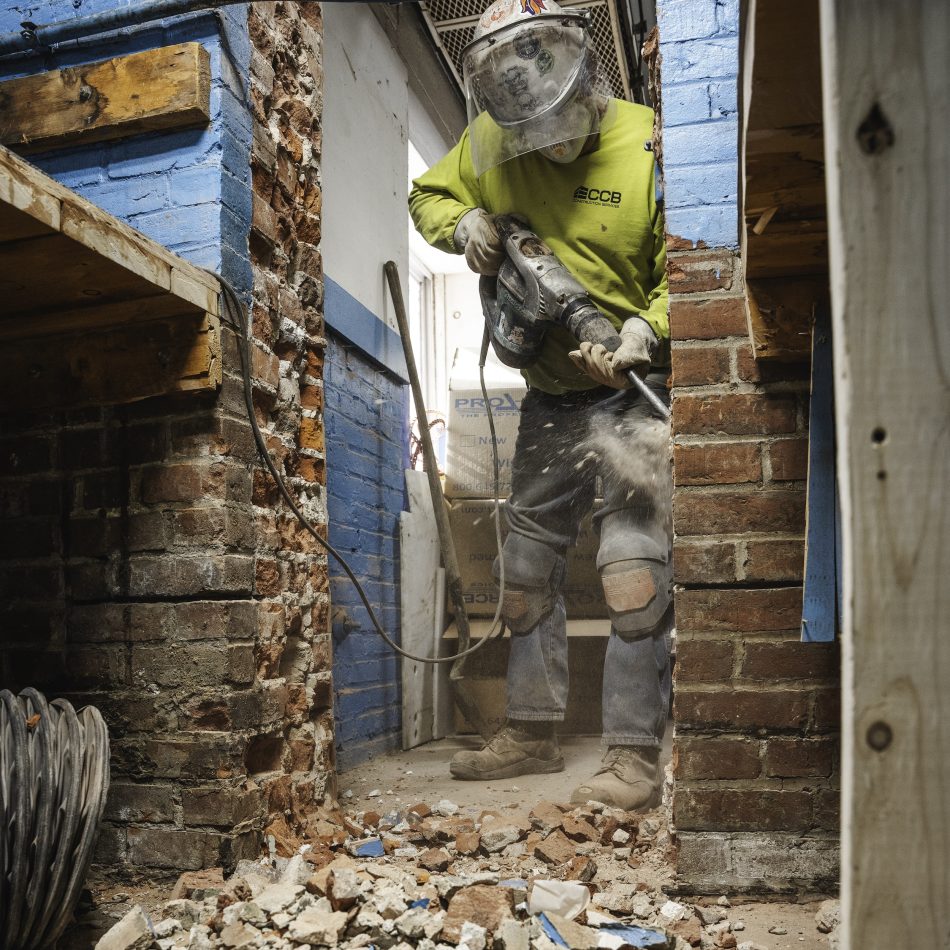 A worker demolishing a brick wall