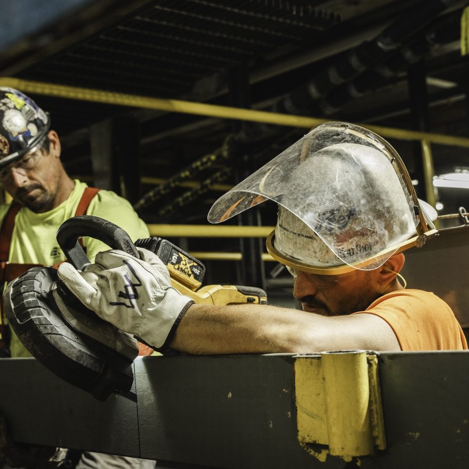 A worker cutting metal while another looks on